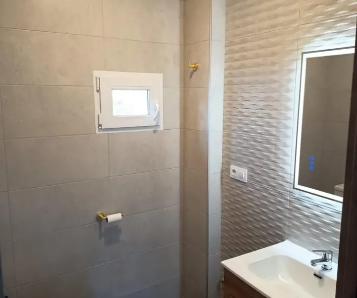 Baño con ducha, revestimiento claro y mueble de lavabo